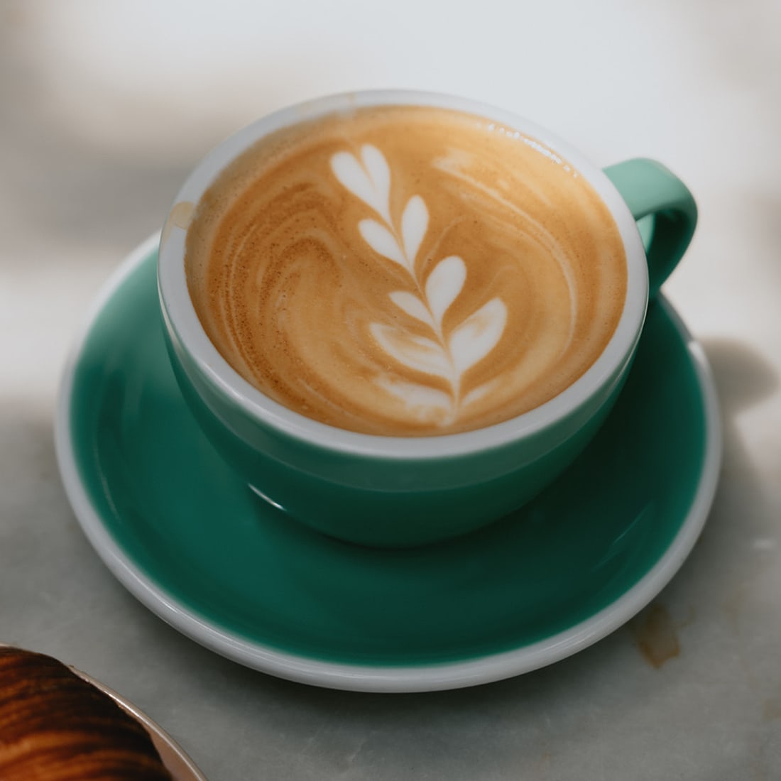 A latte with leaf latte art in a green cup